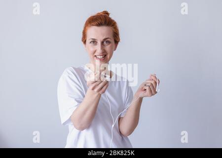 Nice young girl redhead with headphones laughing looking at camera over white background. Stock Photo