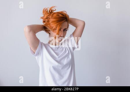 Horizontal portrait of pleasant-looking Caucasian female with long hair,  wearing white casual T-shirt, covering her face with hair, looking happily i Stock Photo