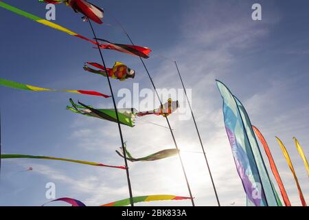 Colorful ribbons and kite figures hanging on poles and flying on blue sky background kite festival Stock Photo