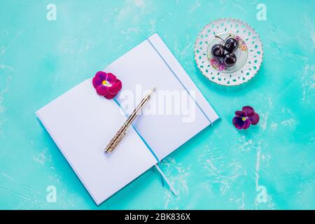 Pen and open blank notebook mock up on blue background decorated with cherry berry.styled elegant desk top. Copy space.concept of new ideas, to do Stock Photo