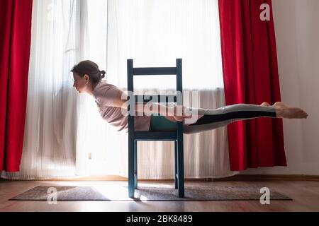 Young woman practicing yoga in Superman Pose or Viparita Shalabhasana using chair Stock Photo