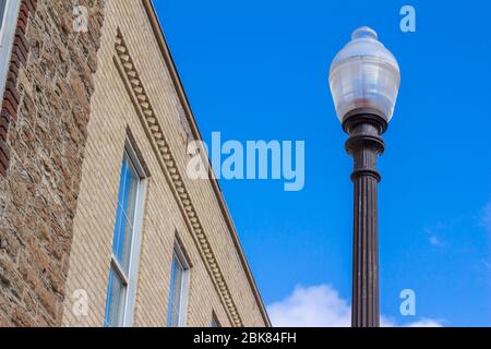 Close upward view of an attractive city street light pole, next to a traditional vintage brick building, with blue sky background Stock Photo