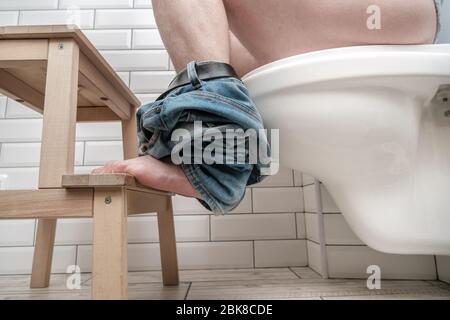 Man sitting on toilet bowl properly, he put feet on a small stool in a squatting position, during the defecation. Health concept. Stock Photo