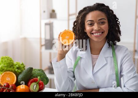 Cheerful female dietician holding fresh orange half Stock Photo