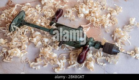 an old green vintage / antique hand drill for carpentry on the workbench in wood chips Stock Photo