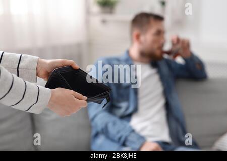 Woman holding empty wallet, drunk man alcoholic on background Stock Photo