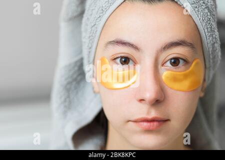 Portrait of a beautiful young girl with golden patches under her eyes. After a shower with a towel on his head on a gray background. Stock Photo