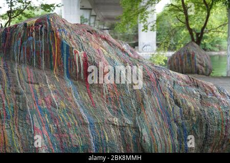 A big stone on the river bank covered paint all over with thin stripes of various colors. An abstract decoration of a free standing boulder. Stock Photo