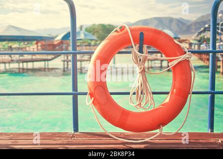 Orange lifebuoy with rope on a wooden pier near sea. Important safety equipment for lifesaving in river, lake and beach. Stock Photo