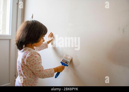 Little happy girl learns to paint the wall Stock Photo