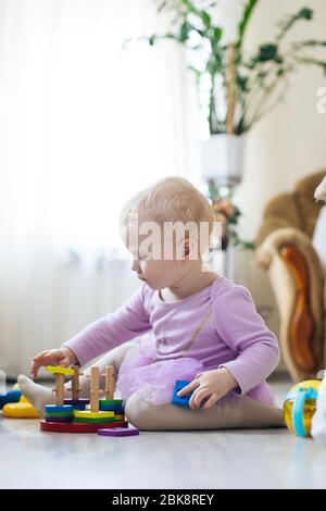 girl plays toys in living room. Montessori wooden toy folded pyramid. Circle, quadra, triangle, rectangle wooden elements of children's toys. Multi-co Stock Photo