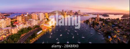 Sydney harbour around Lavender bay across city CBD and the Harbour bridge at sunset in aerial wide panorama. Stock Photo