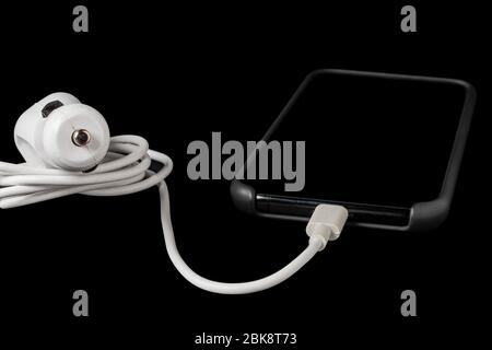 horizontal view of a mobile phone connected to a white color car lighter isolated on black background Stock Photo