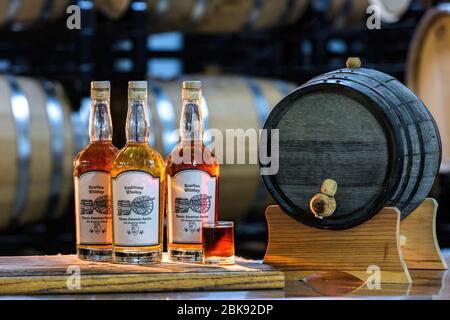 Bottles of whiskey on a table next to a small barrel in a cellar Stock Photo