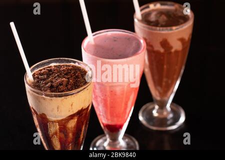 Three glasses of various milkshakes (chocolate, strawberry and vanilla) on wood background Stock Photo