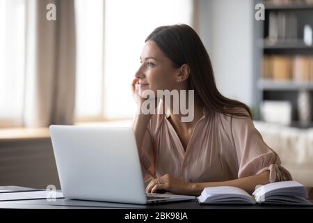 Dreamy young woman pondering ideas, sitting at desk with laptop Stock Photo