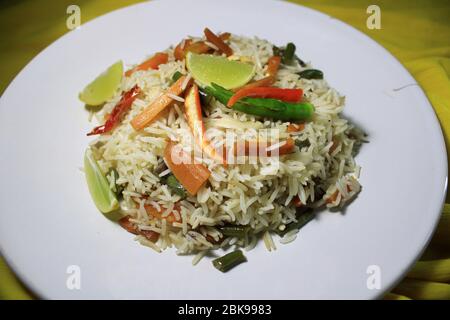 Vegetable fried rice on white plate with lemon and chili. Top view. Fried Rice on the white plate isolated on yellow cloth background. Stock Photo