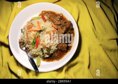 Vegetable fried rice with chili chicken on white plate isolated on yellow cloth. Top view. Chili chicken is a popular Indo-Chinese dish Stock Photo