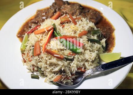 Vegetable fried rice with chili chicken on white plate isolated on yellow cloth. Top view. Chili chicken is a popular Indo-Chinese dish Stock Photo