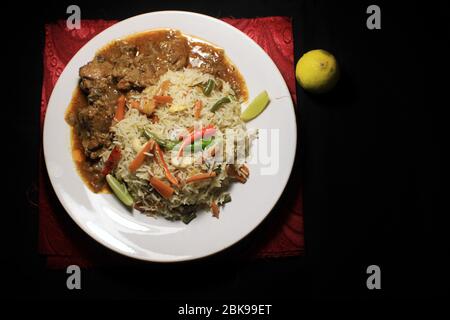 Vegetable fried rice & chili chicken on white plate with lemon and chili isolated on black background. Top view. Chili chicken is a popular Indo-Chine Stock Photo