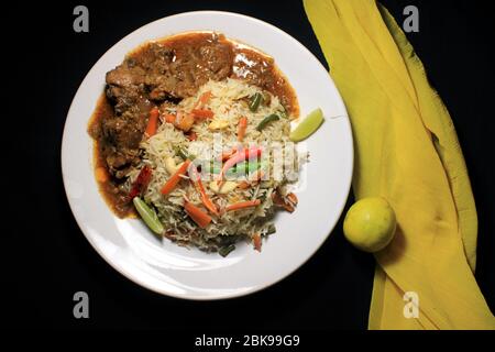 Vegetable fried rice & chili chicken on white plate with lemon and chili isolated on black background. Top view. Chili chicken is a popular Indo-Chine Stock Photo