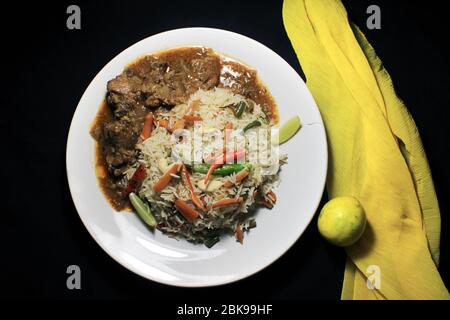 Vegetable fried rice & chili chicken on white plate with lemon and chili isolated on black background. Top view. Chili chicken is a popular Indo-Chine Stock Photo