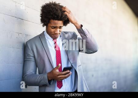 Worried Black Businessman using his smartphone outdoors. Stock Photo