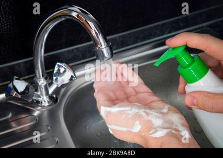 Wash your hands. a young guy washes his hands with soap under the faucet over a metal sink on a black dark background. Virus prevention. Hygienic proc Stock Photo