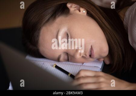 Close up tired woman sleeping at workplace, lying on notebook Stock Photo
