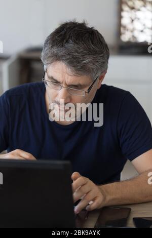Vertical portrait of a middle age man with eye glasses working from home using black laptop. Stock Photo