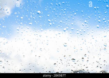 Raindrops on window glass against blue sky with white clouds Stock Photo