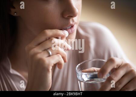Close up young woman taking pill, holding water glass Stock Photo