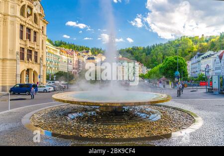 Karlovy Vary, Czech Republic, May 10, 2019: Hot spring geyser Vridlo at Carlsbad historical city centre, Tepla river embankment, colorful beautiful buildings, West Bohemia, Czech Republic