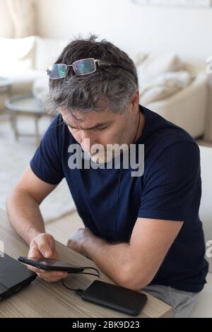 Vertical portrait of a middle age man wearing eye glasses and deep blue t-shirt checking his smartphone Stock Photo