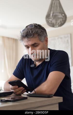 Vertical portrait of a middle age man wearing eye glasses and deep blue t-shirt checking his smartphone Stock Photo