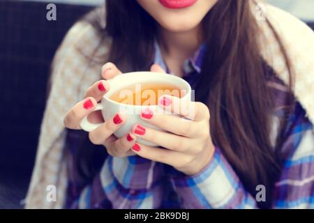 Girl wrapped in a blanket holding a cup of tea close-up in outdoor cafe Stock Photo