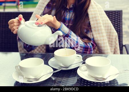 Woman hands pours tea from a teapot into a cups in outdoor cafe Stock Photo