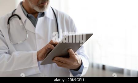 Old male doctor using digital tablet computer in hospital, closeup Stock Photo