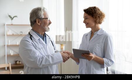 Happy senior male doctor physician handshaking young female nurse Stock Photo