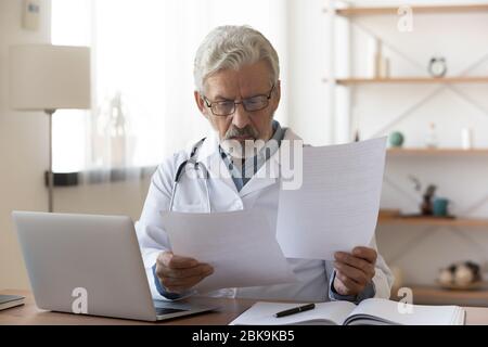 Serious professional senior doctor checking medical documents at workplace Stock Photo