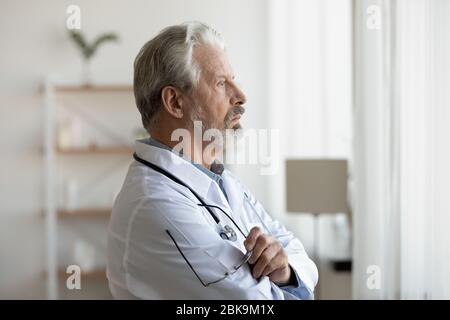 Thoughtful serious senior doctor looking through window lost in thoughts Stock Photo