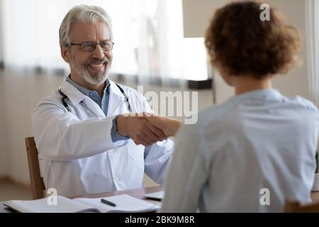 Smiling professional physician handshaking female patient at medical consultation Stock Photo