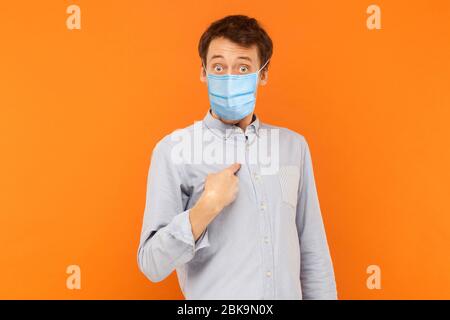 Who? me? Portrait of shocked young worker man with surgical medical mask standing pointing himself, asking and looking at camera with amazed face. ind Stock Photo