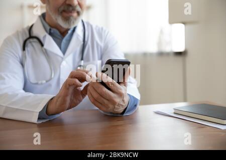 Senior male doctor using mobile phone technology apps at desk Stock Photo