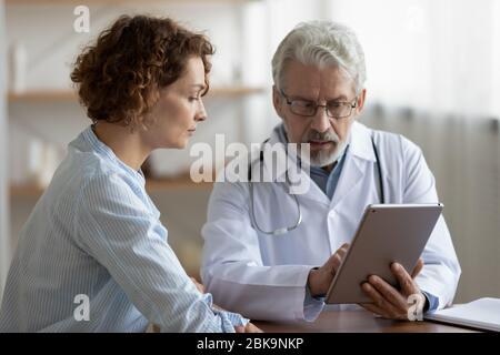Older doctor consulting young female patient using digital tablet Stock Photo