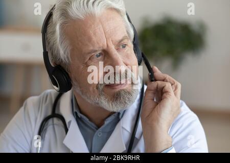 Smiling older physician wearing headset with microphone looking away Stock Photo