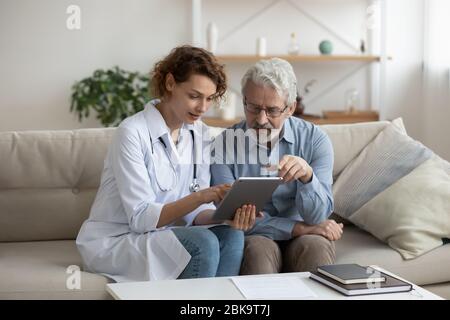 Female doctor using digital tablet consulting senior patient at home Stock Photo