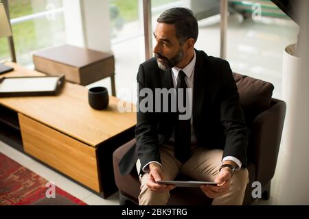 Handsome elegant mature business man using multitasking multimedia digital tablet in the office Stock Photo