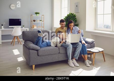 Happy family watching together video online in a laptop while sitting comfortably at home. Stock Photo