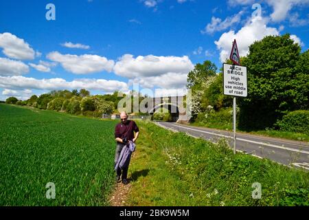 Man walking through a field in West Wycombe, Buckinghamshire, UK, away from the railway bridge over the main Wycombe Road A4010 Stock Photo